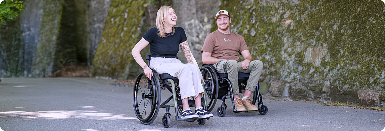 A young woman and a young man sit in wheelchairs and look at each other.